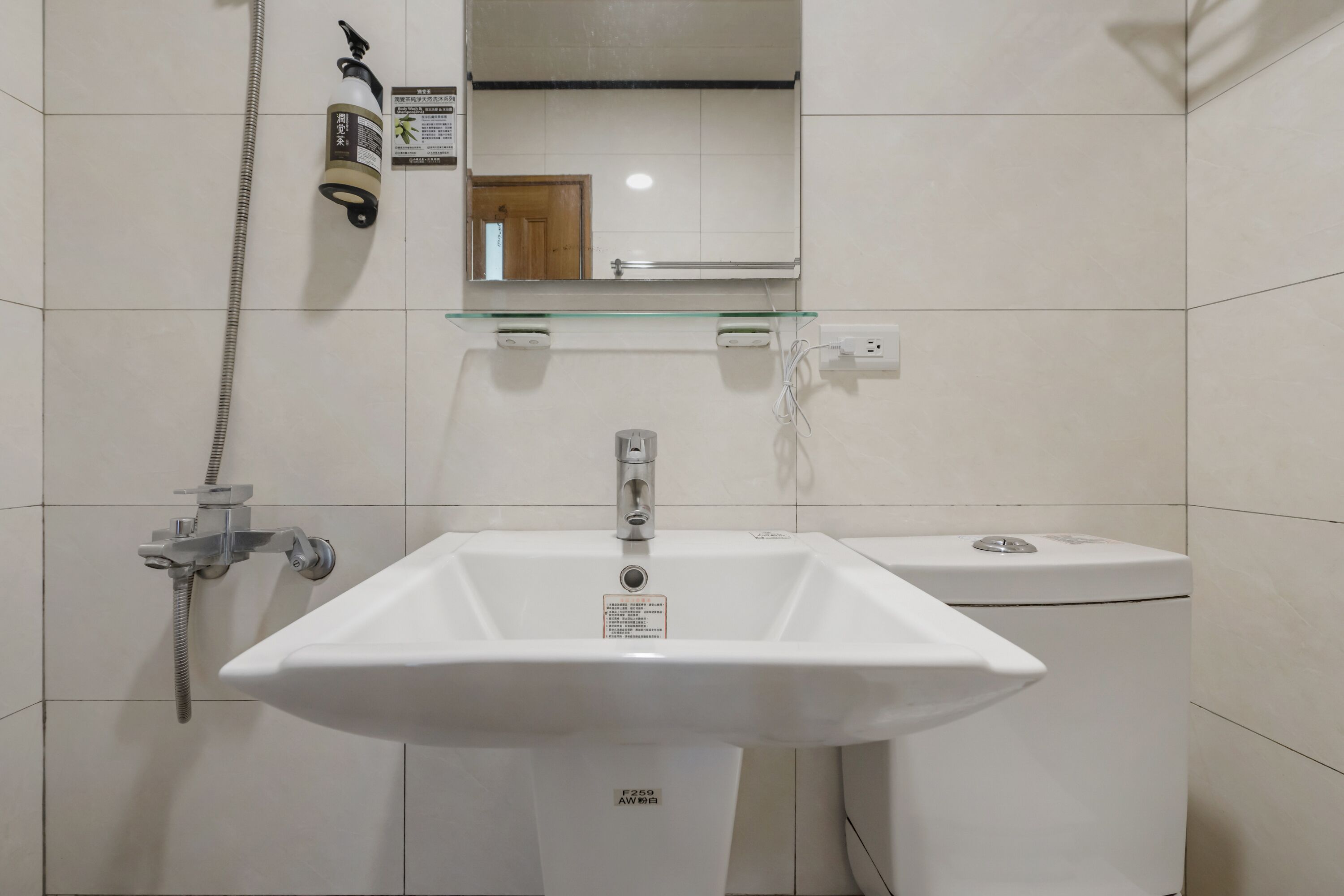 A bathroom with a white sink, a glass shelf, a mirror, and a shower.