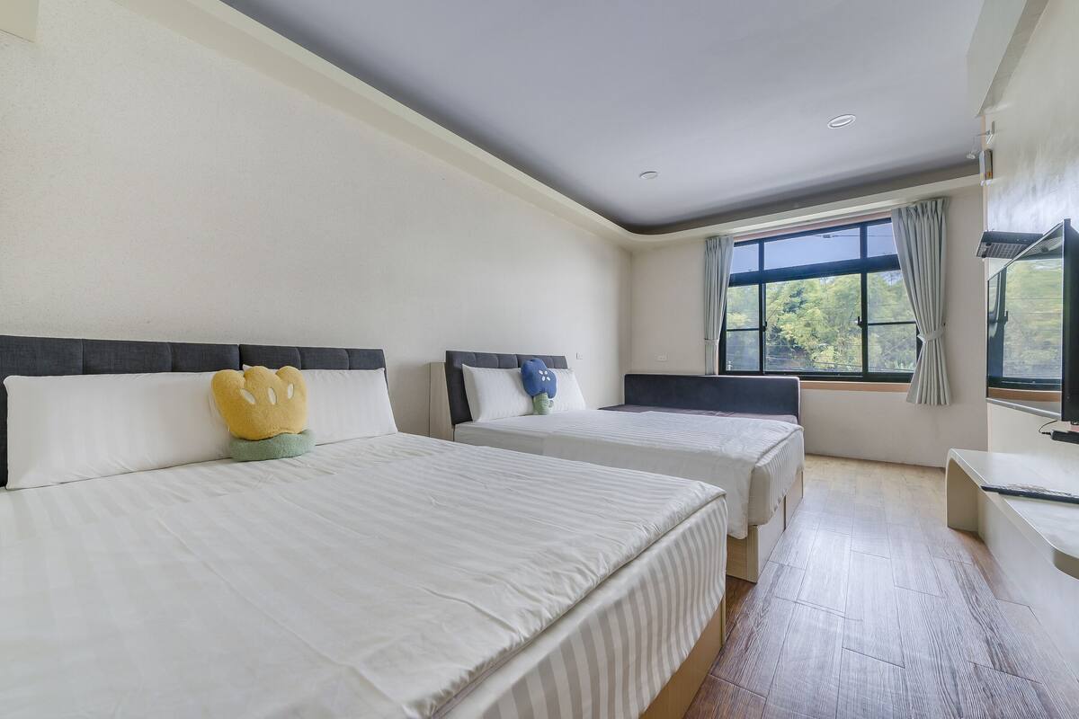 Quarto de hotel com duas camas, uma janela grande e uma televisão.