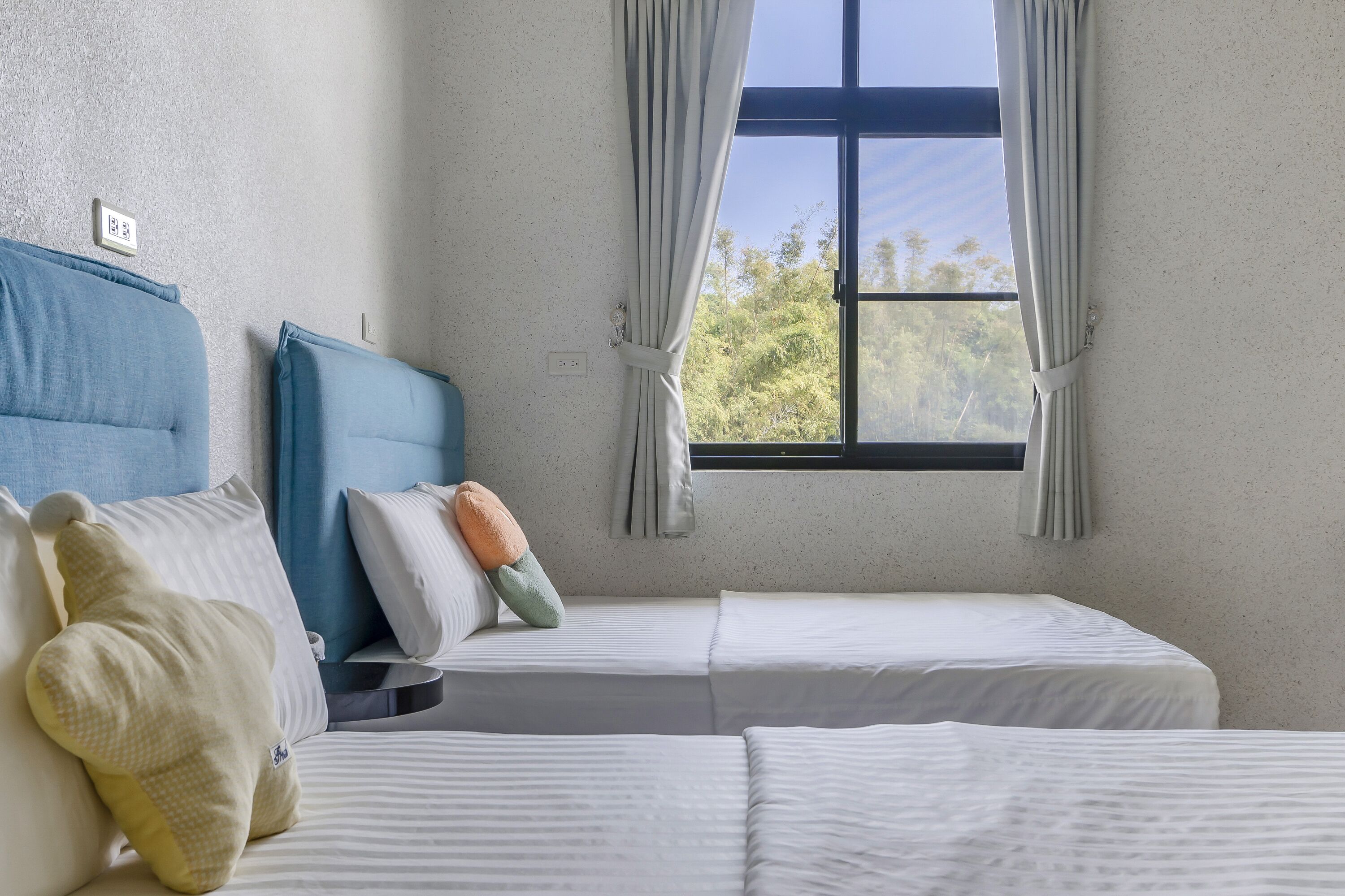 Une chambre avec deux lits, une fenêtre avec des rideaux et une prise électrique au mur.
