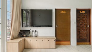 A room with a large flat-screen TV mounted on the wall, a wooden desk with a computer and a coffee maker, and two doors with signs. - Bo Ya Homestay (Liuqiu)