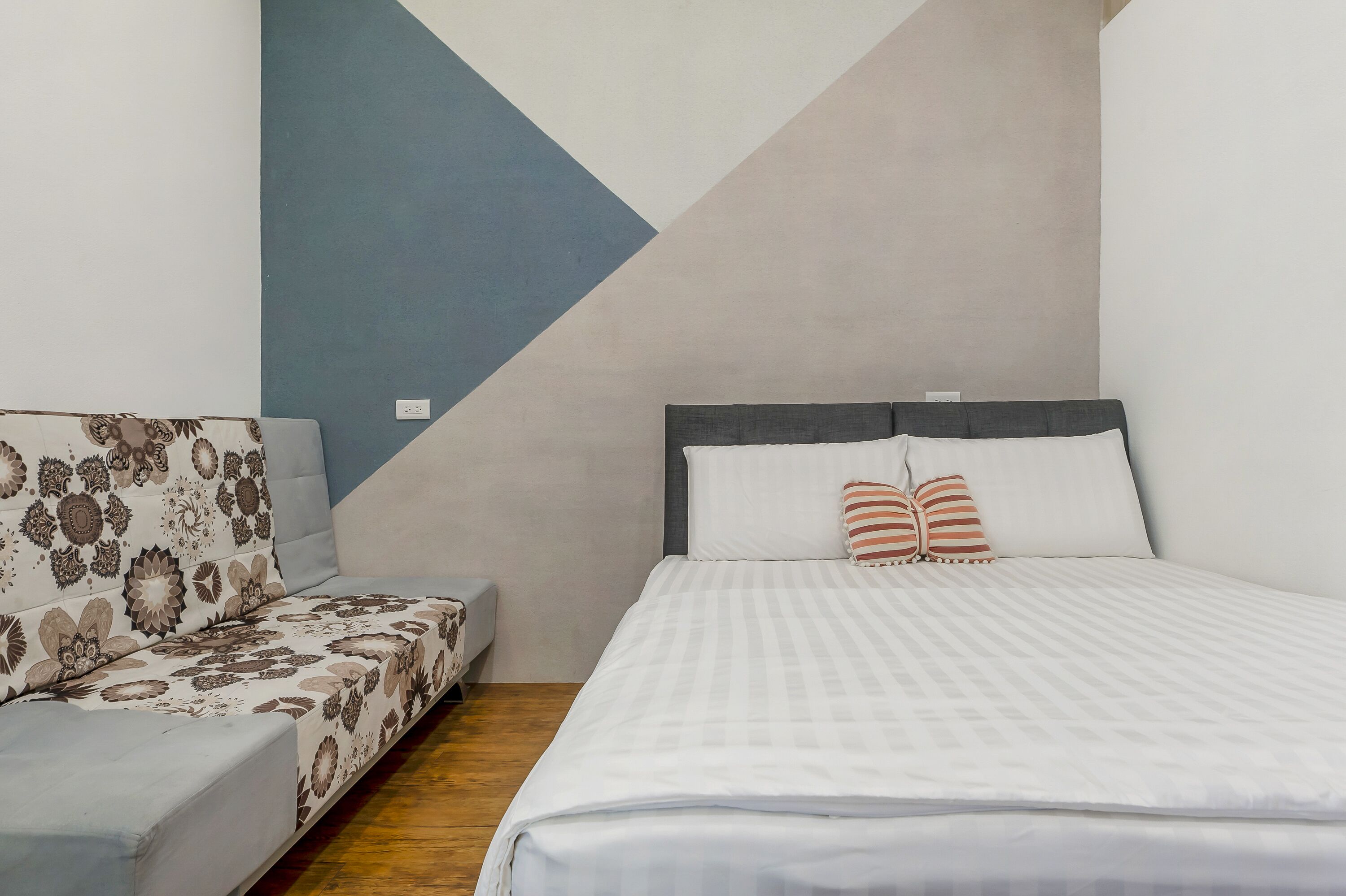 Une chambre à coucher comprenant un lit, un canapé et un mur orné d’un motif géométrique.
