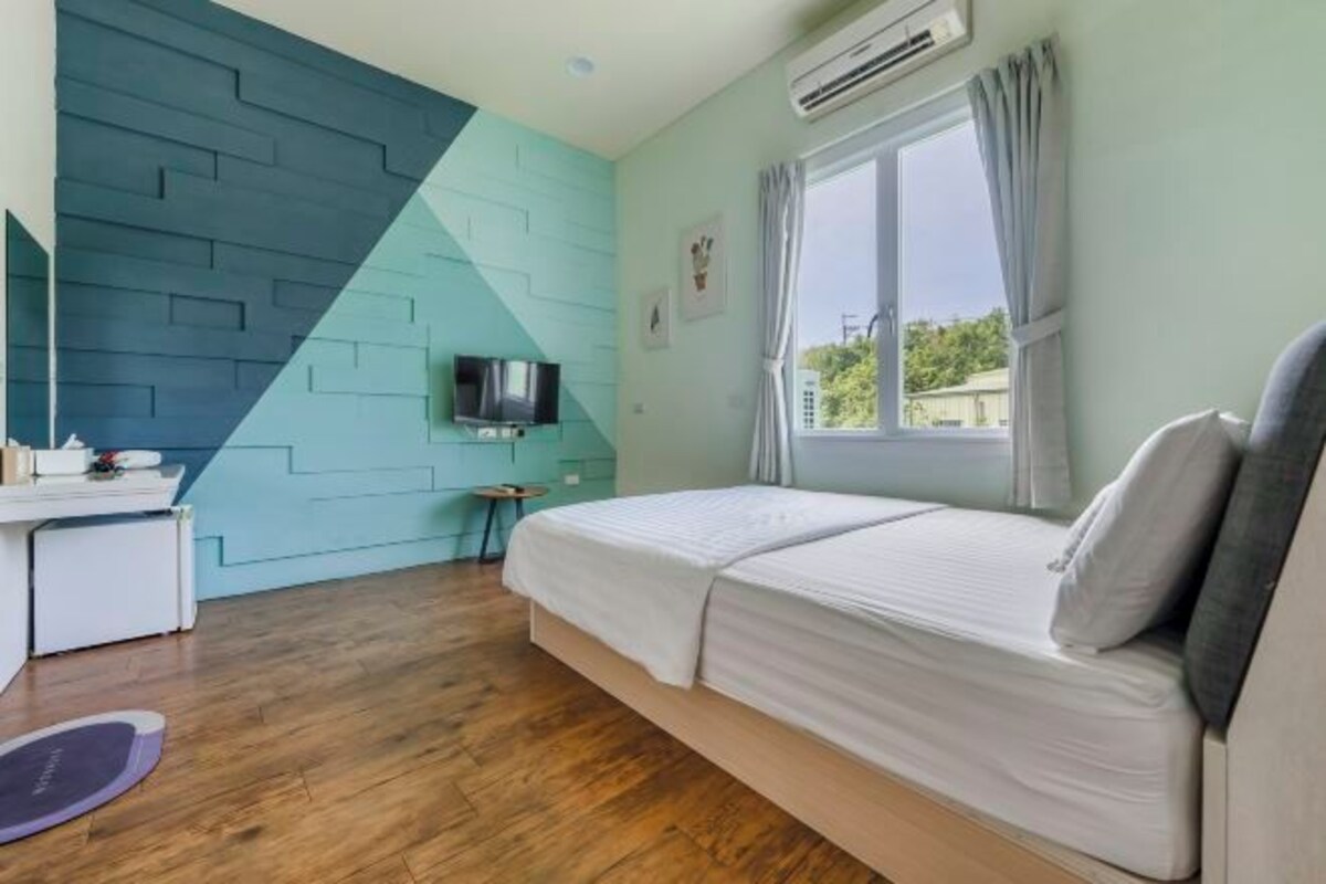 Un dormitorio con cama, escritorio, televisor y ventana con cortinas.