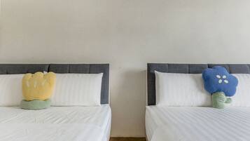 Dos camas con cabeceros grises y ropa de cama blanca, cada una con un cojín diferente.