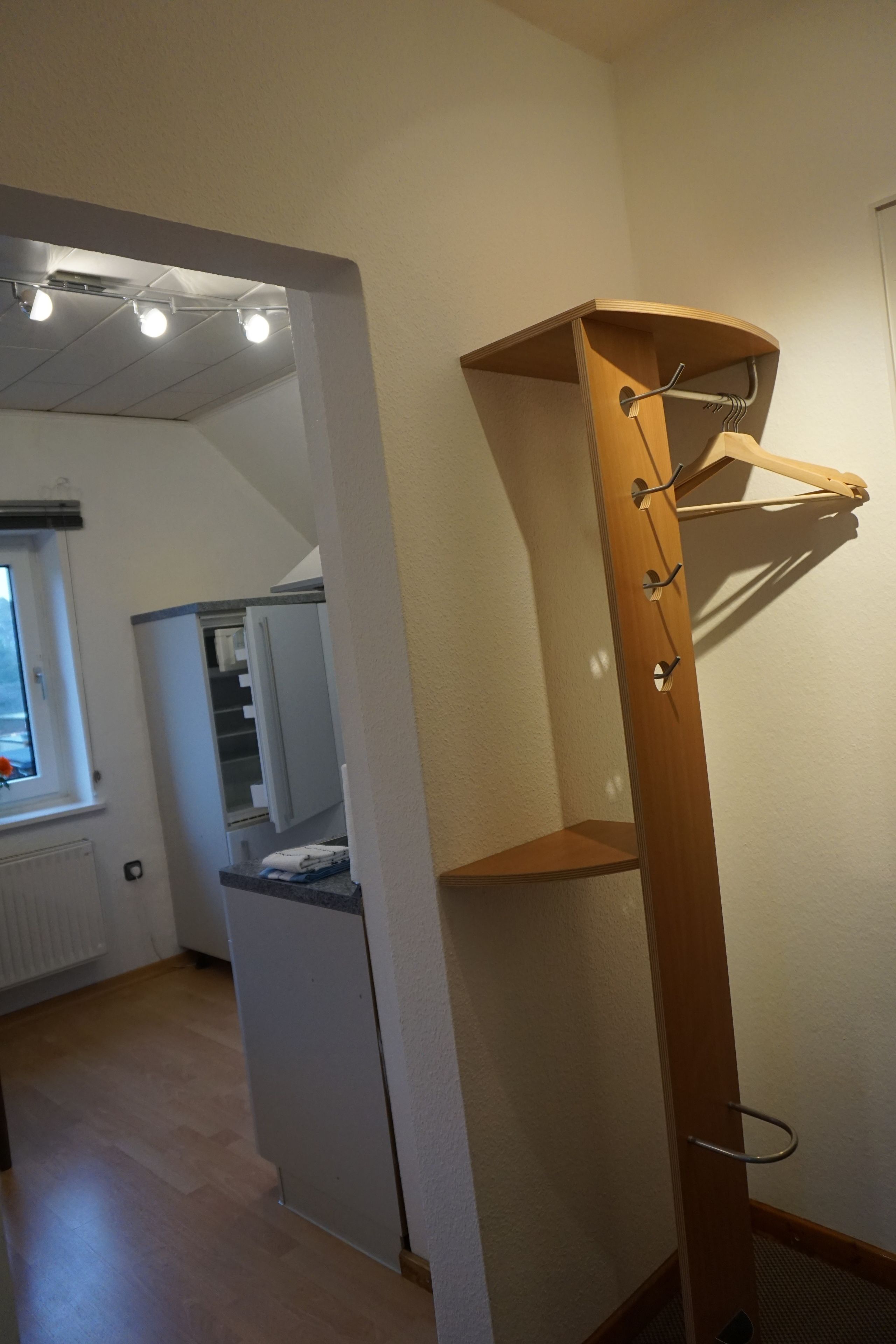 A corner of a room with a wooden coat rack, a white cabinet, and a window with blinds.