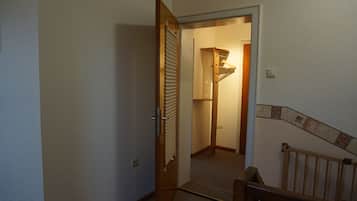 A hallway with a wooden door leading to a room with a radiator and a small shelf.