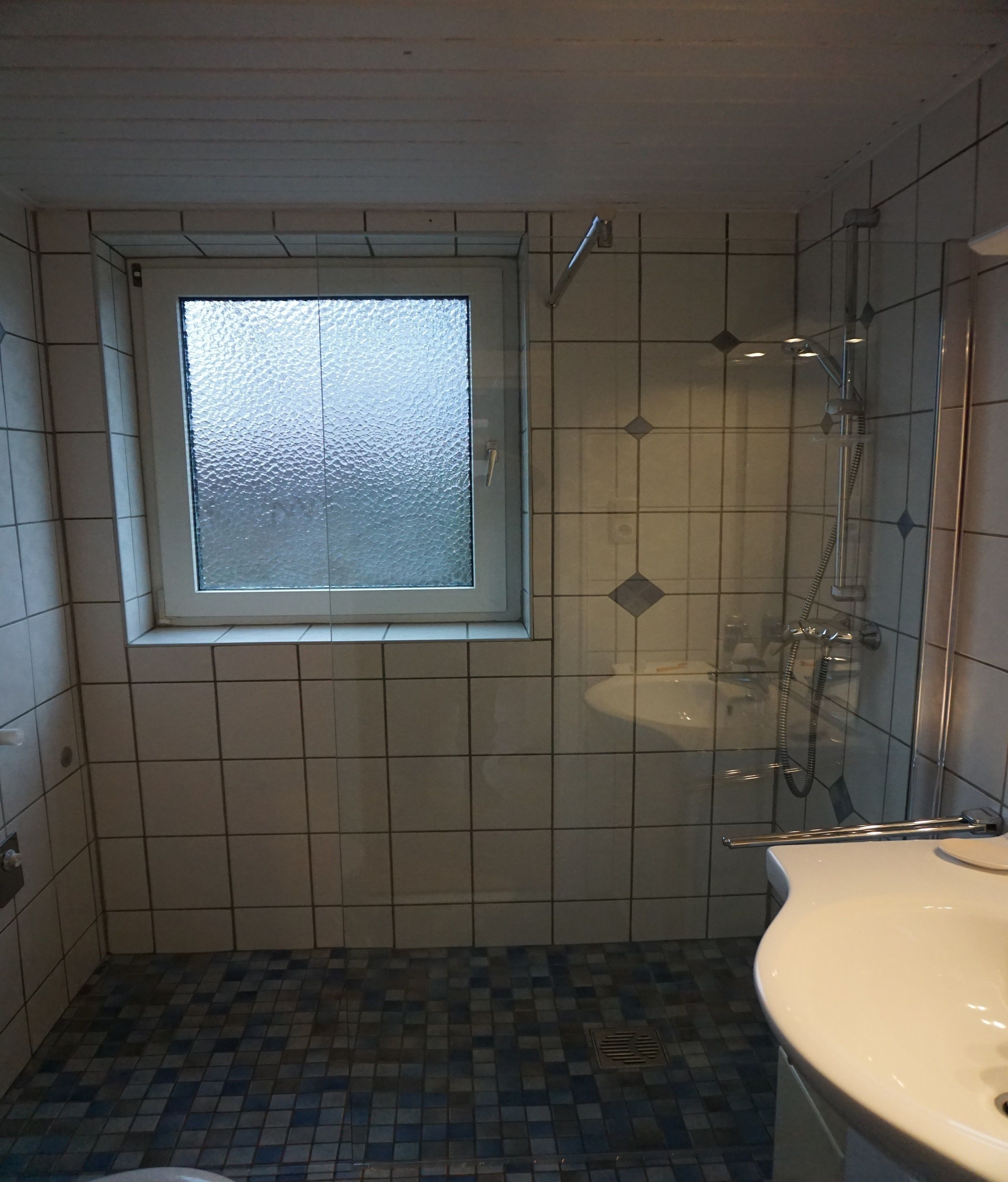 Une salle de bain avec une fenêtre, une douche et un lavabo.