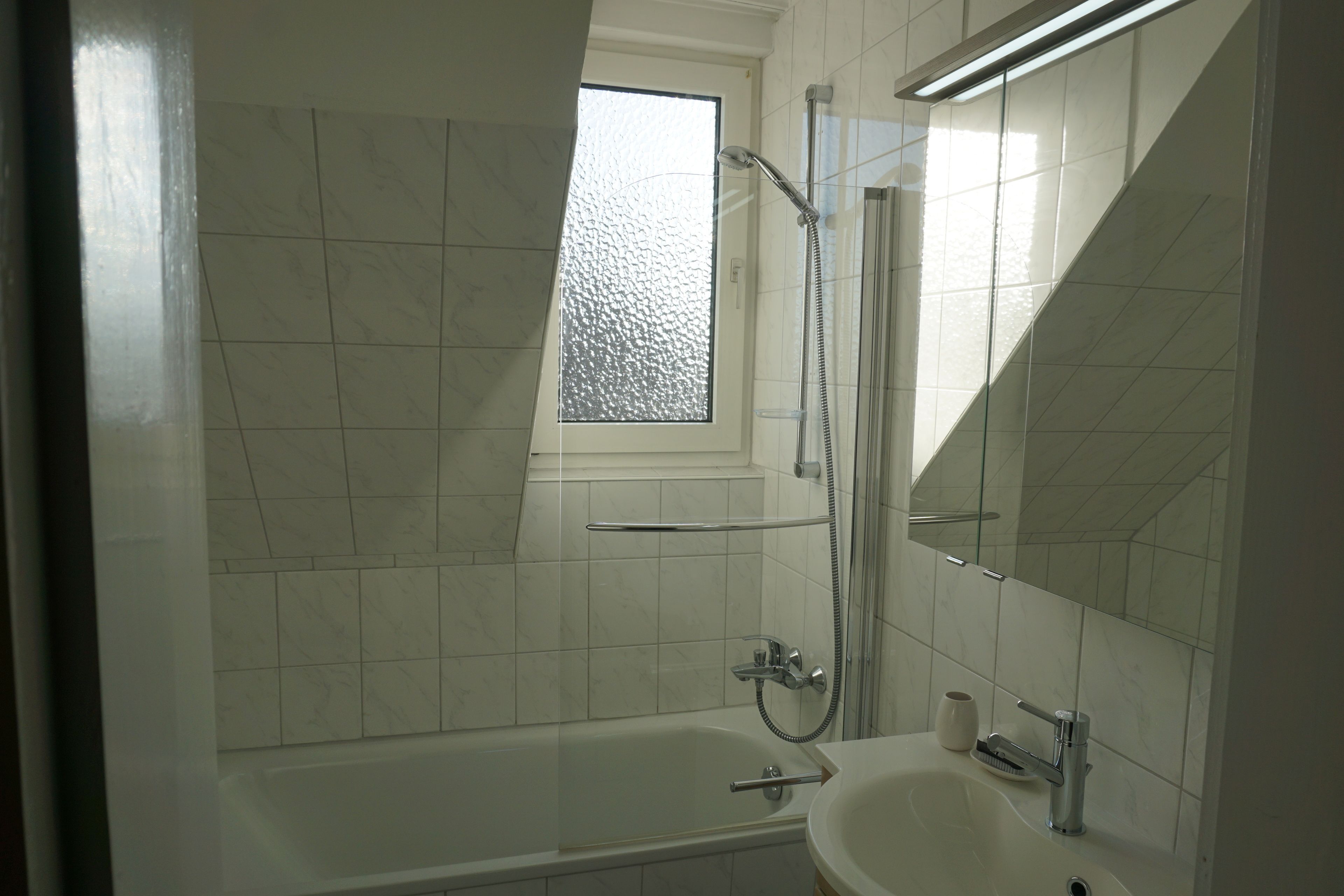 Une salle de bain moderne avec une baignoire, une douche et un lavabo. Il y a une fenêtre au-dessus de la baignoire et un miroir au-dessus du lavabo.