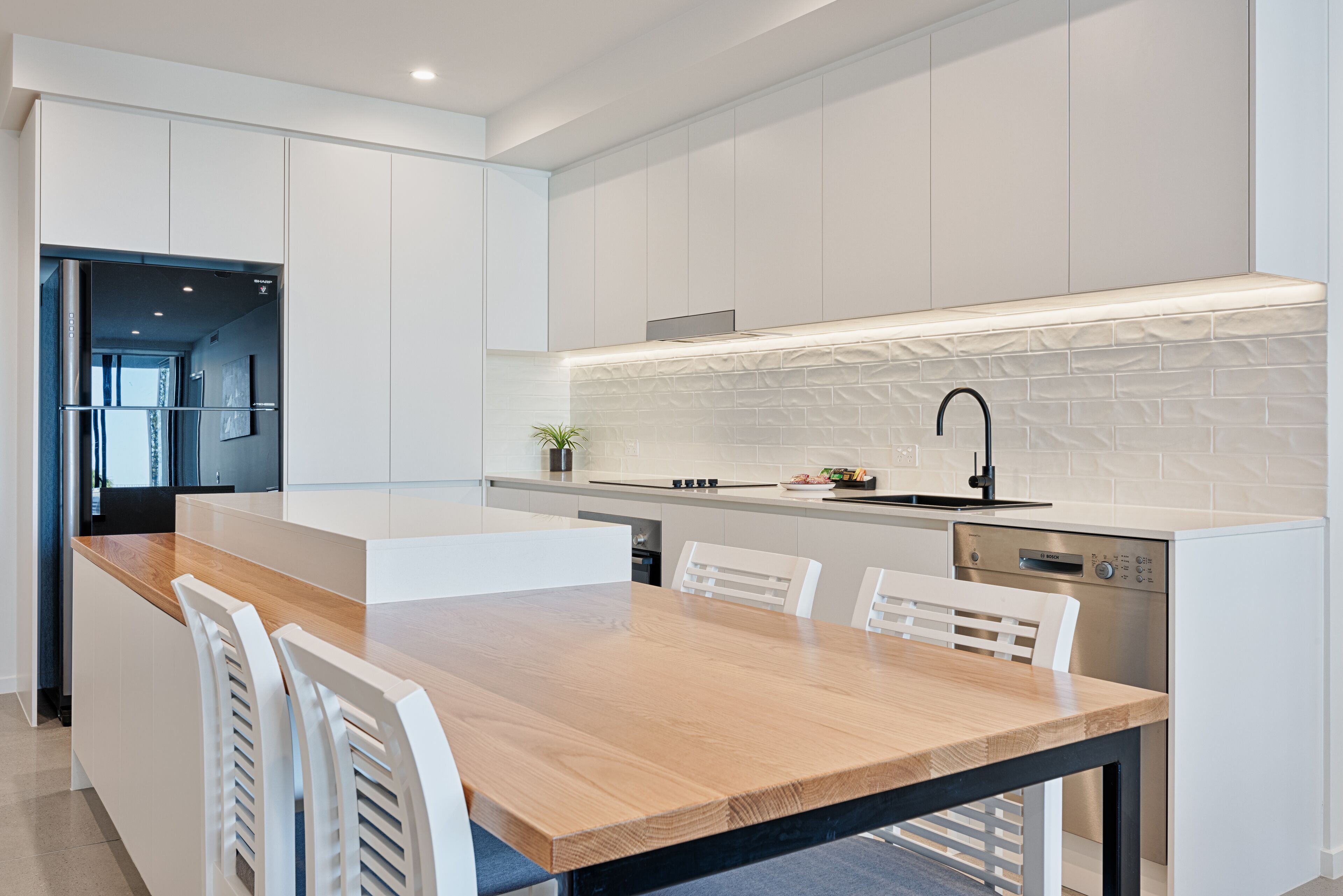Una cocina moderna con armarios blancos, una mesa de comedor de madera y un lavavajillas empotrado.
