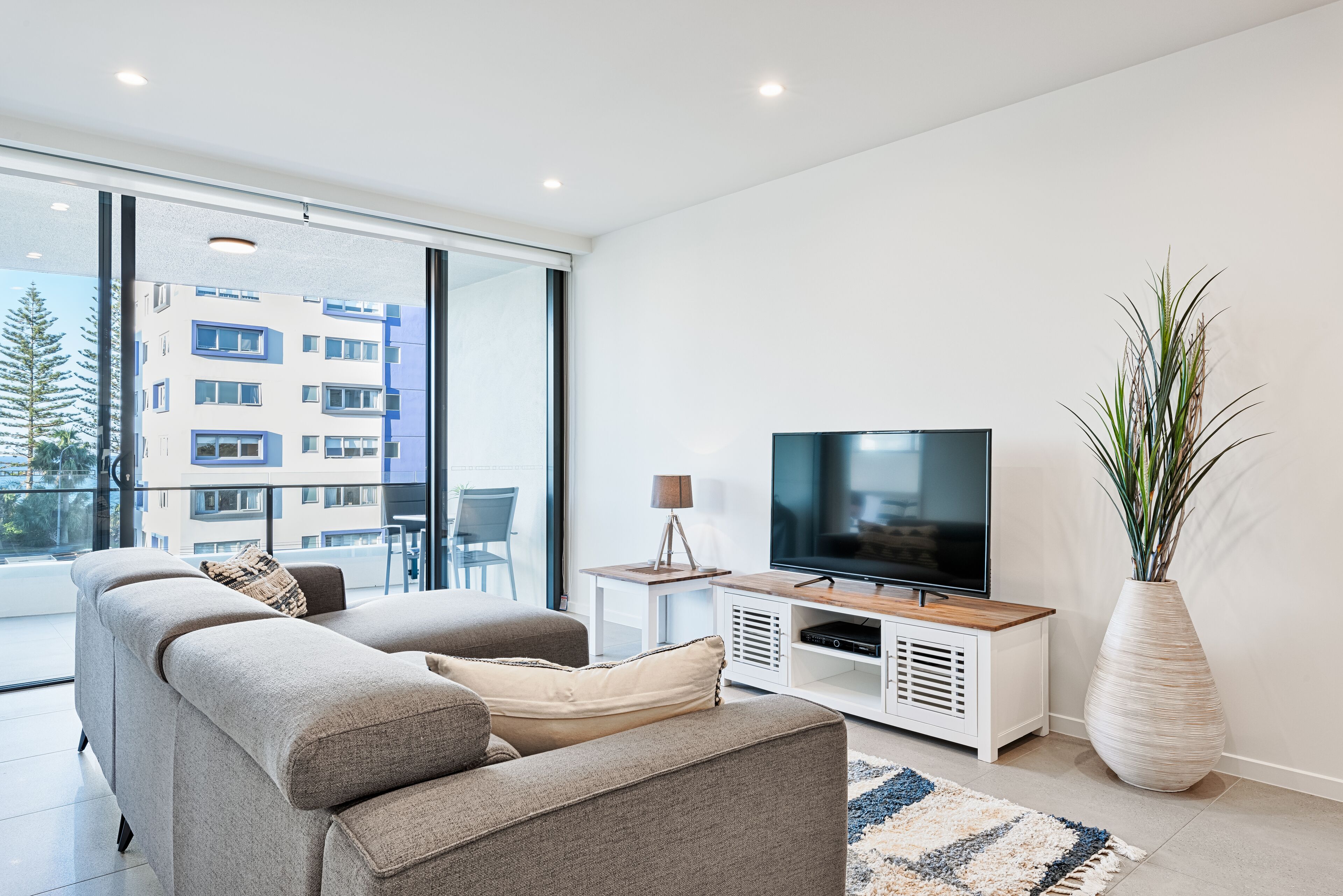 A modern living room with a sofa, TV, and a large window overlooking a building.