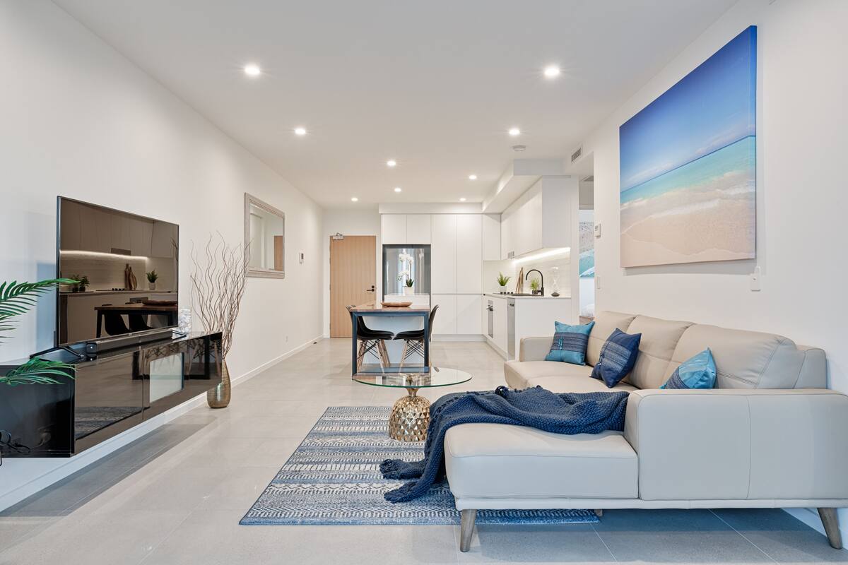 A modern living room with a sofa, a glass coffee table, and a dining area with a table and chairs.
