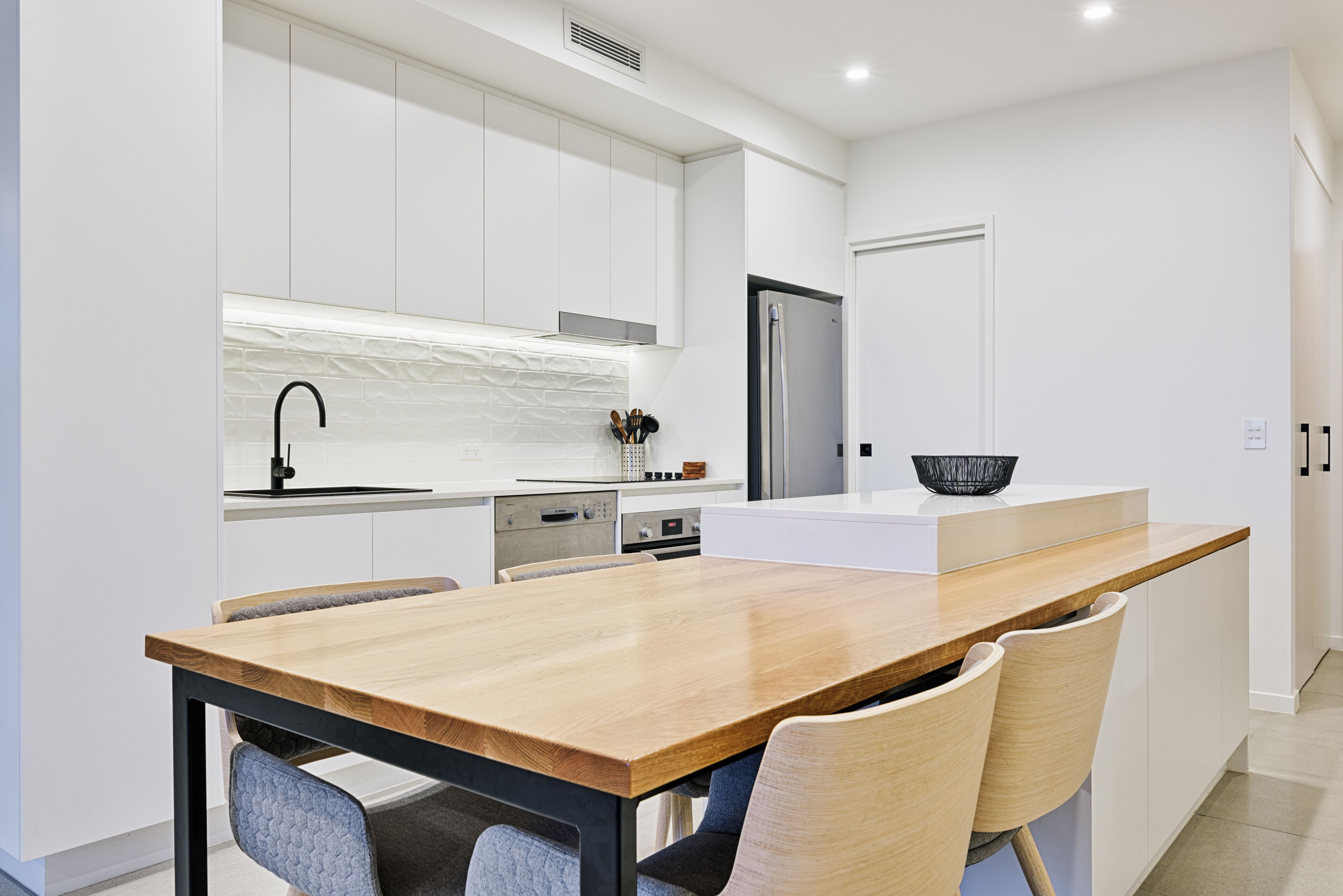 A modern kitchen with white cabinetry, a wooden dining table, and a built-in island with seating.