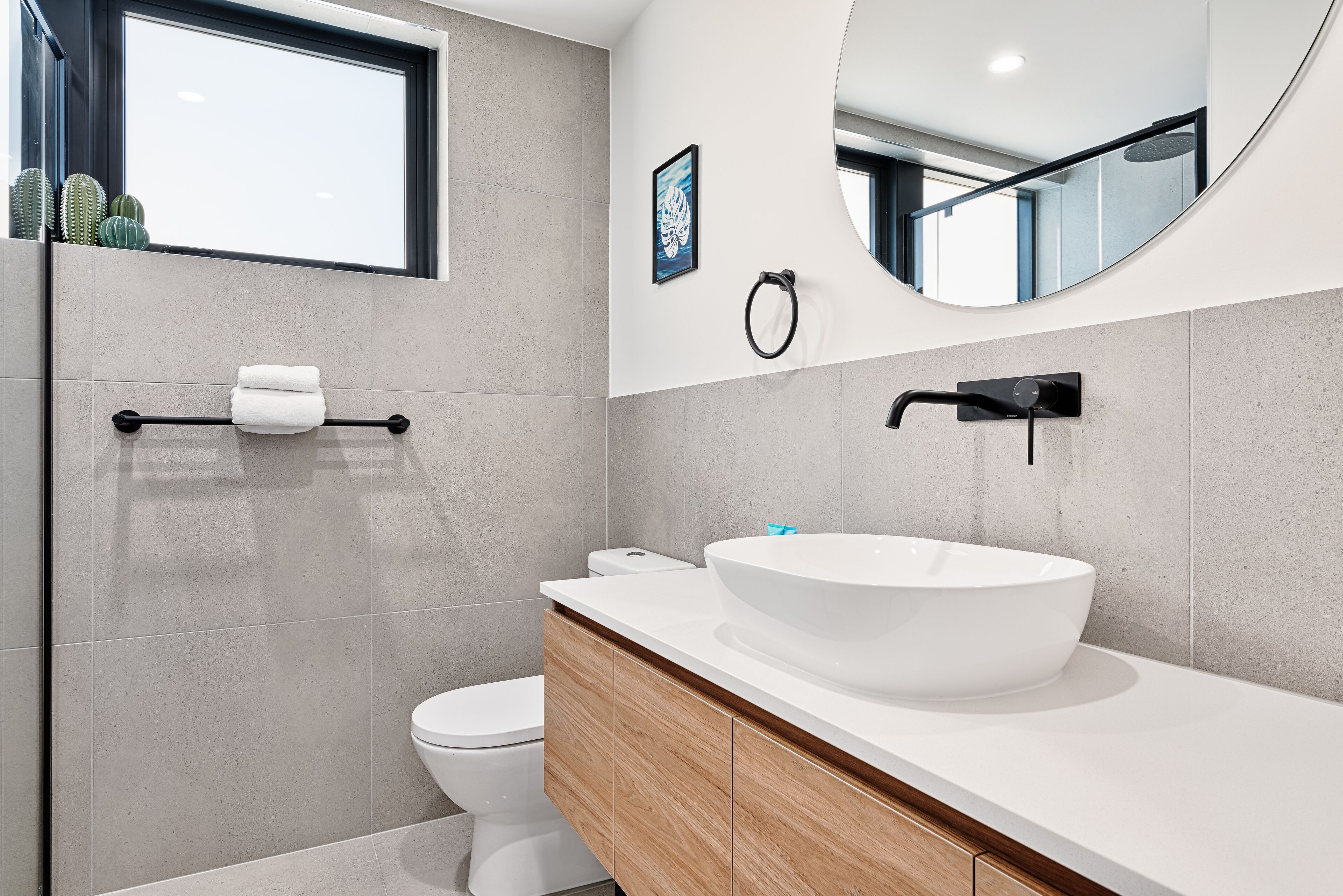A modern bathroom with a large white sink, wooden cabinets, a toilet, and a towel rack.