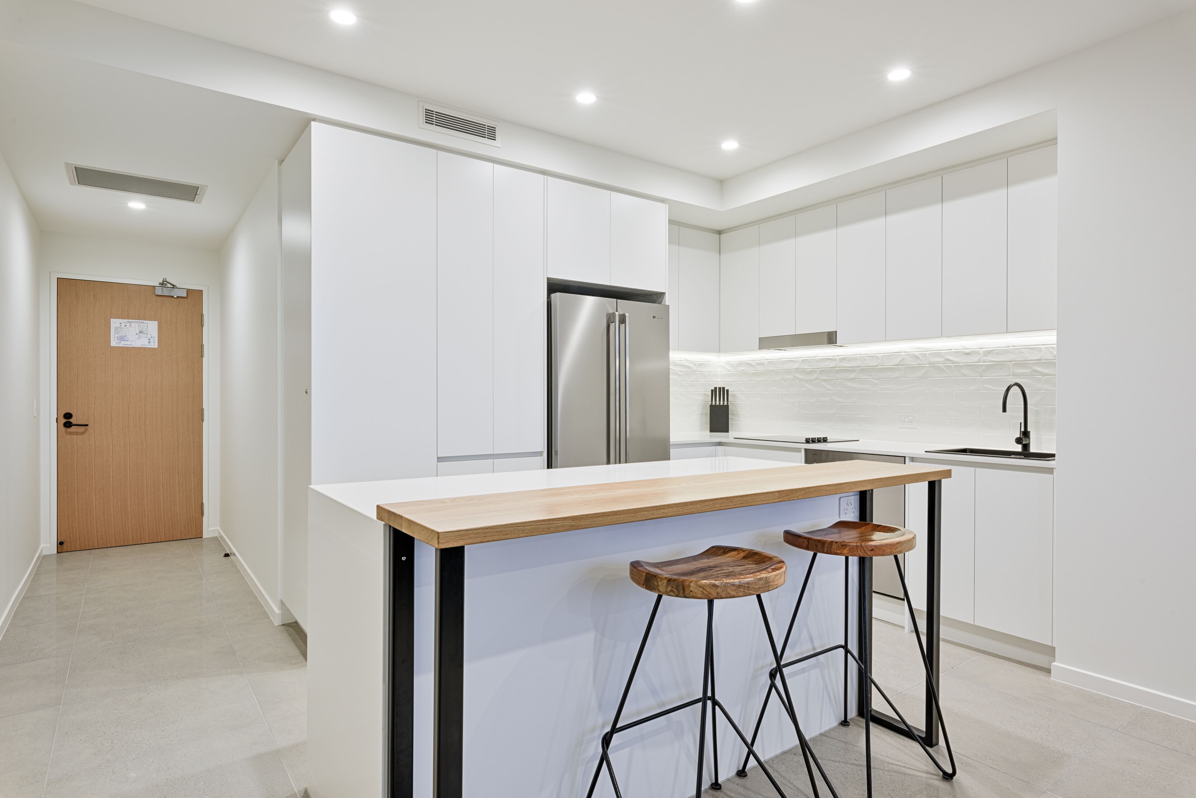 Una cocina moderna con armarios blancos, un refrigerador de acero inoxidable, una encimera de madera y dos taburetes de bar.