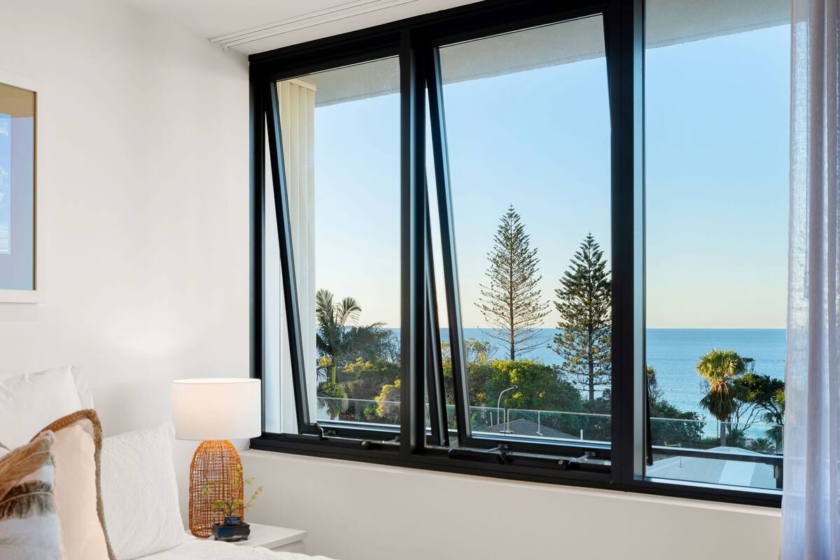 A hotel room with a large window offering a view of the sea and trees.