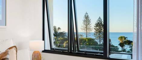 A hotel room with a large window offering a view of the sea and trees.