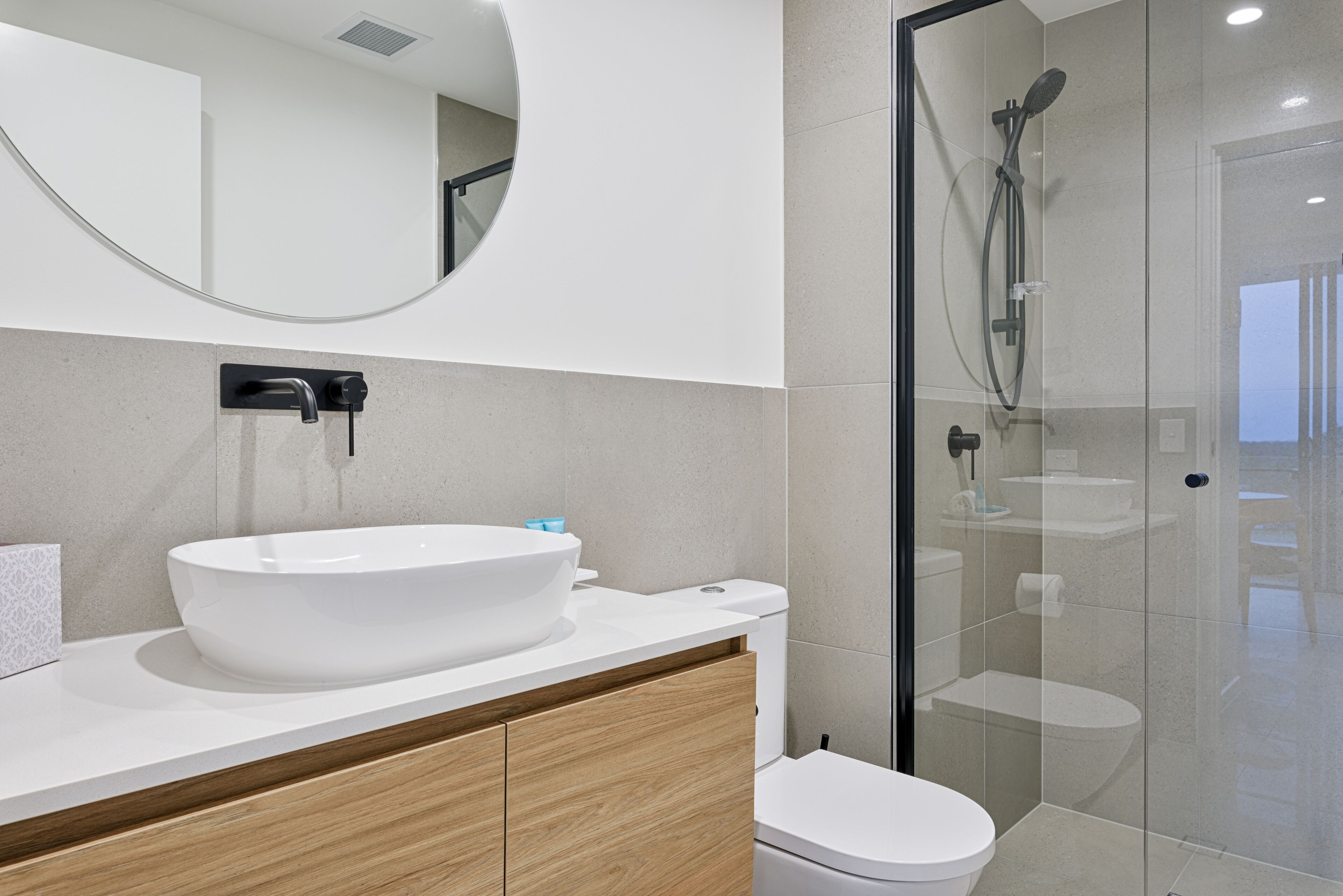 A modern bathroom with a large oval sink, a toilet, and a glass-enclosed shower area.