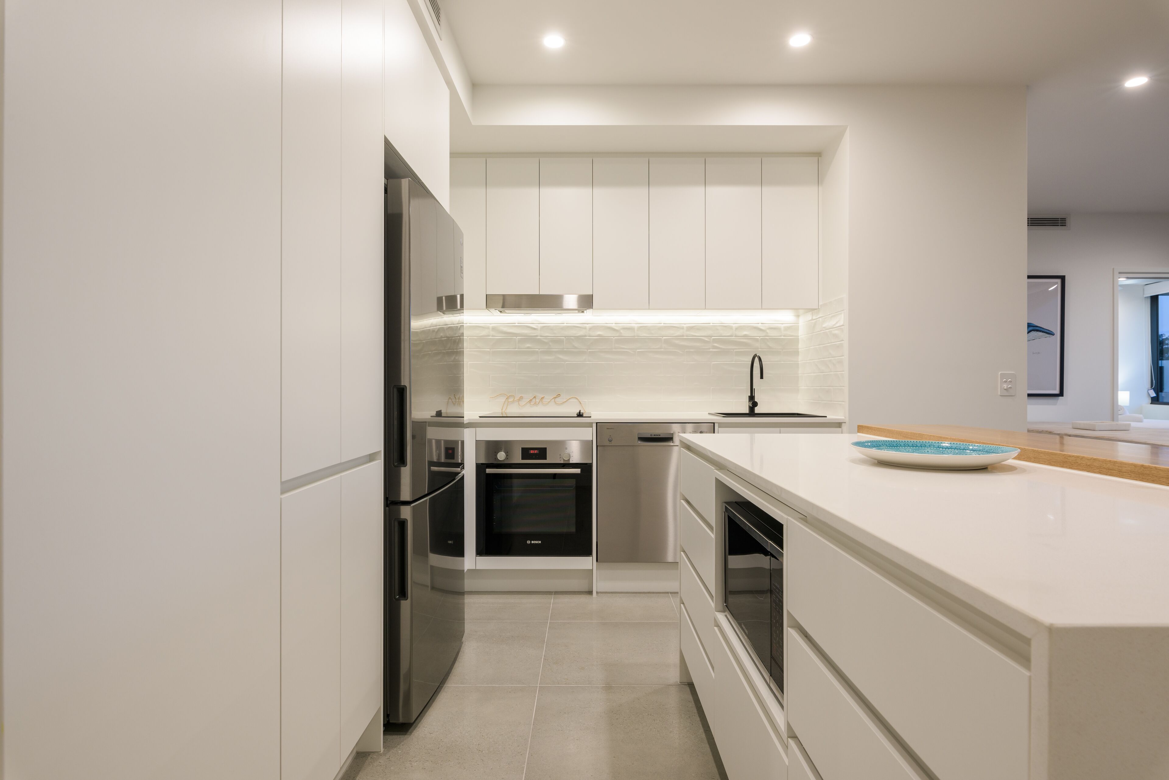 Una cocina moderna con muebles blancos, electrodomésticos de acero inoxidable y una isla grande con un cuenco azul.