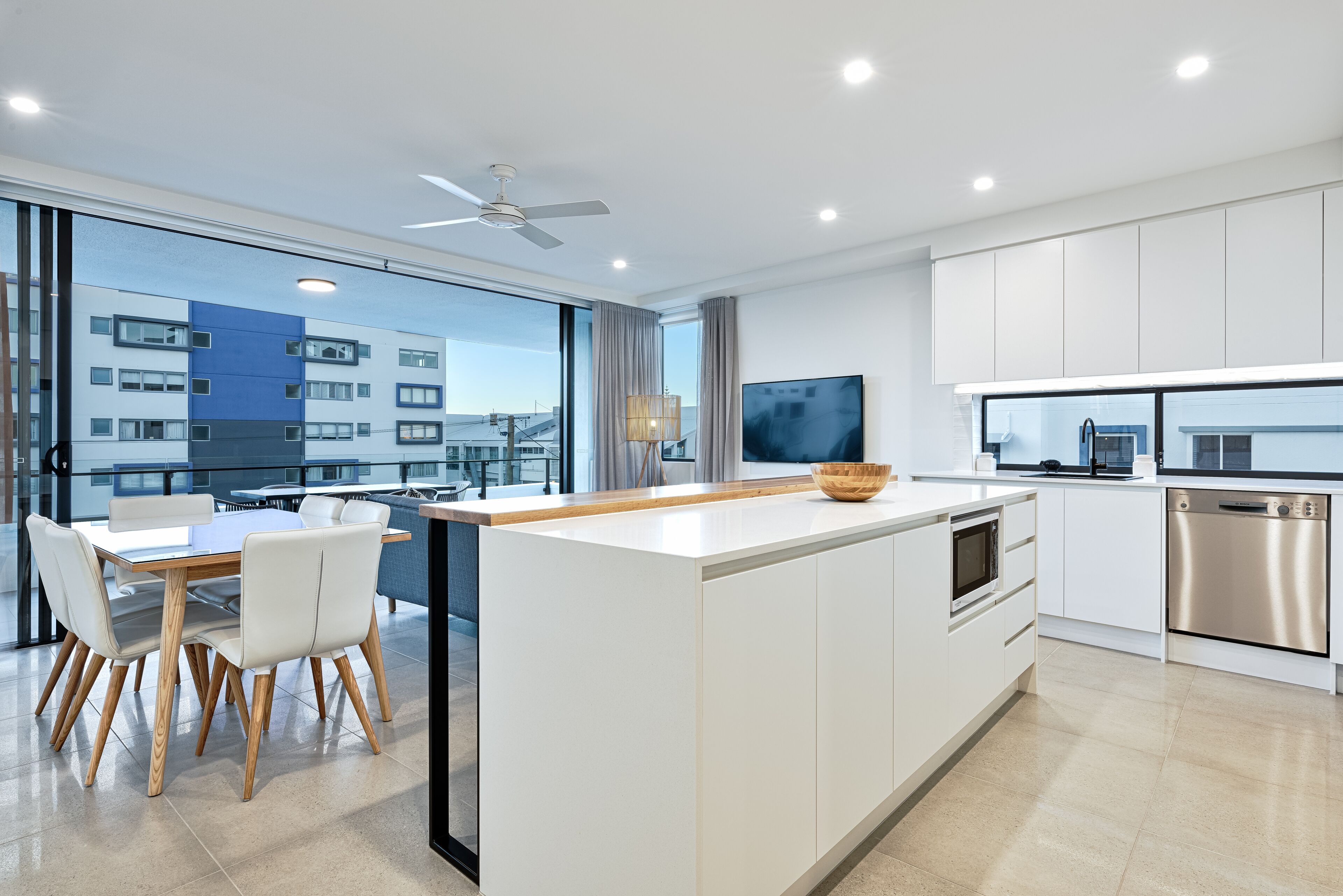 A modern kitchen with a central island, white cabinetry, and a large window overlooking a cityscape.