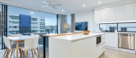 A modern kitchen with a central island, white cabinetry, and a large window overlooking a cityscape.