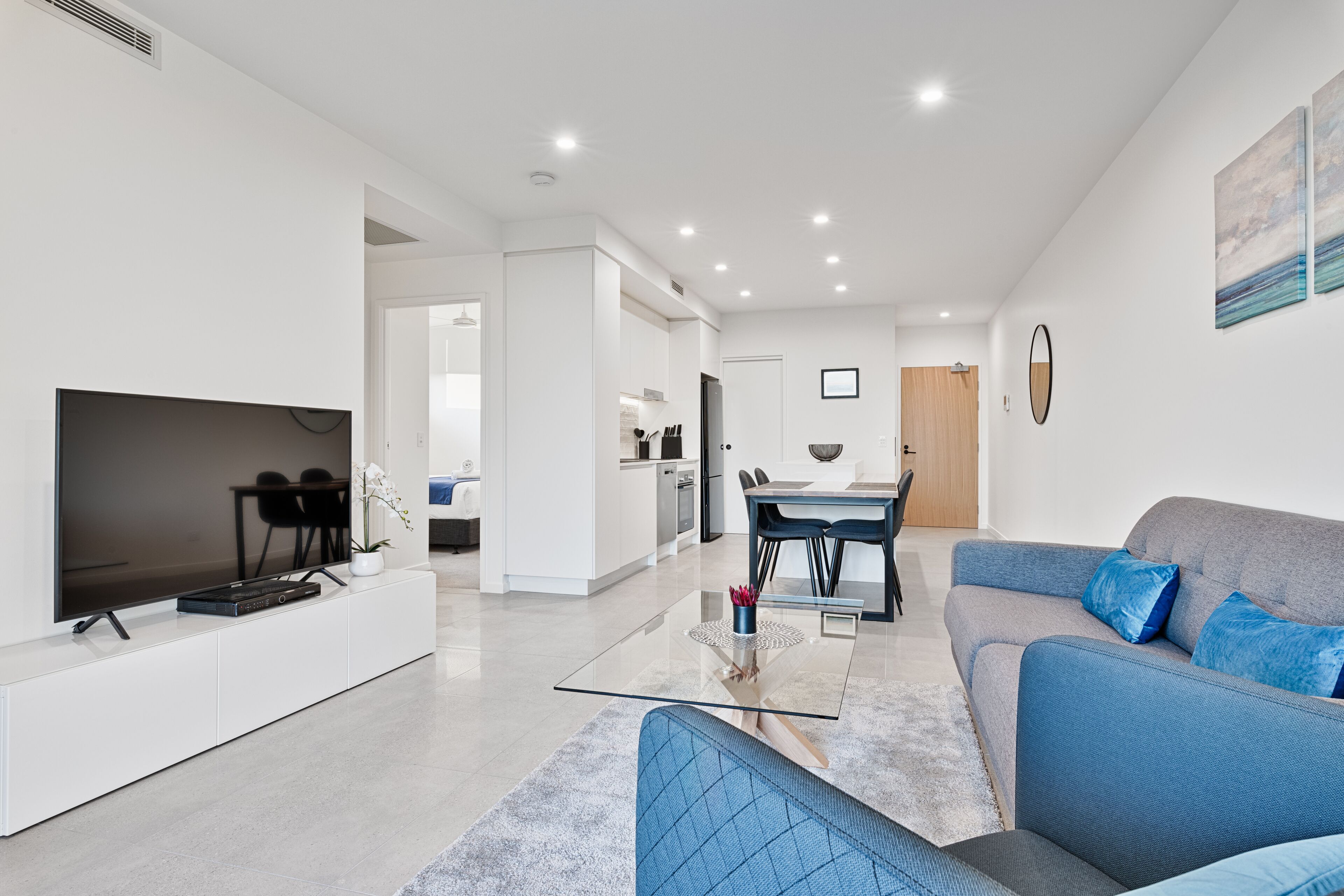 Een moderne woonkamer met een flatscreen televisie, een bank en een eethoek met een tafel en stoelen.