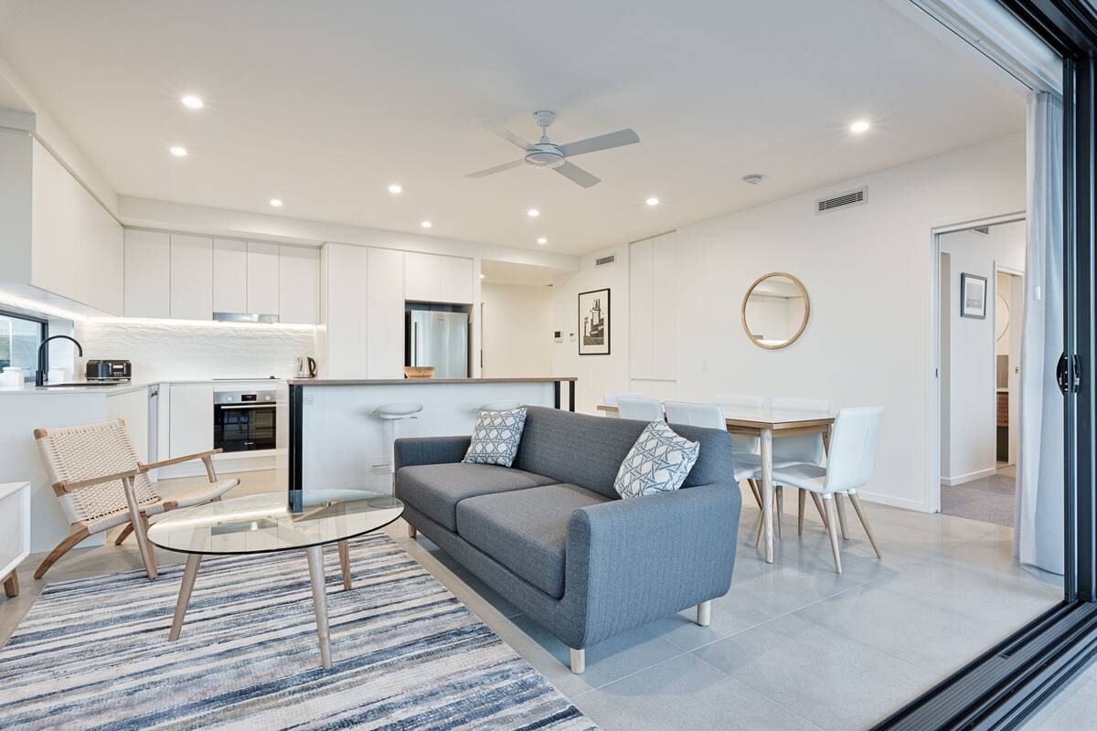 A modern living room with a grey sofa, a glass coffee table, and a striped rug.