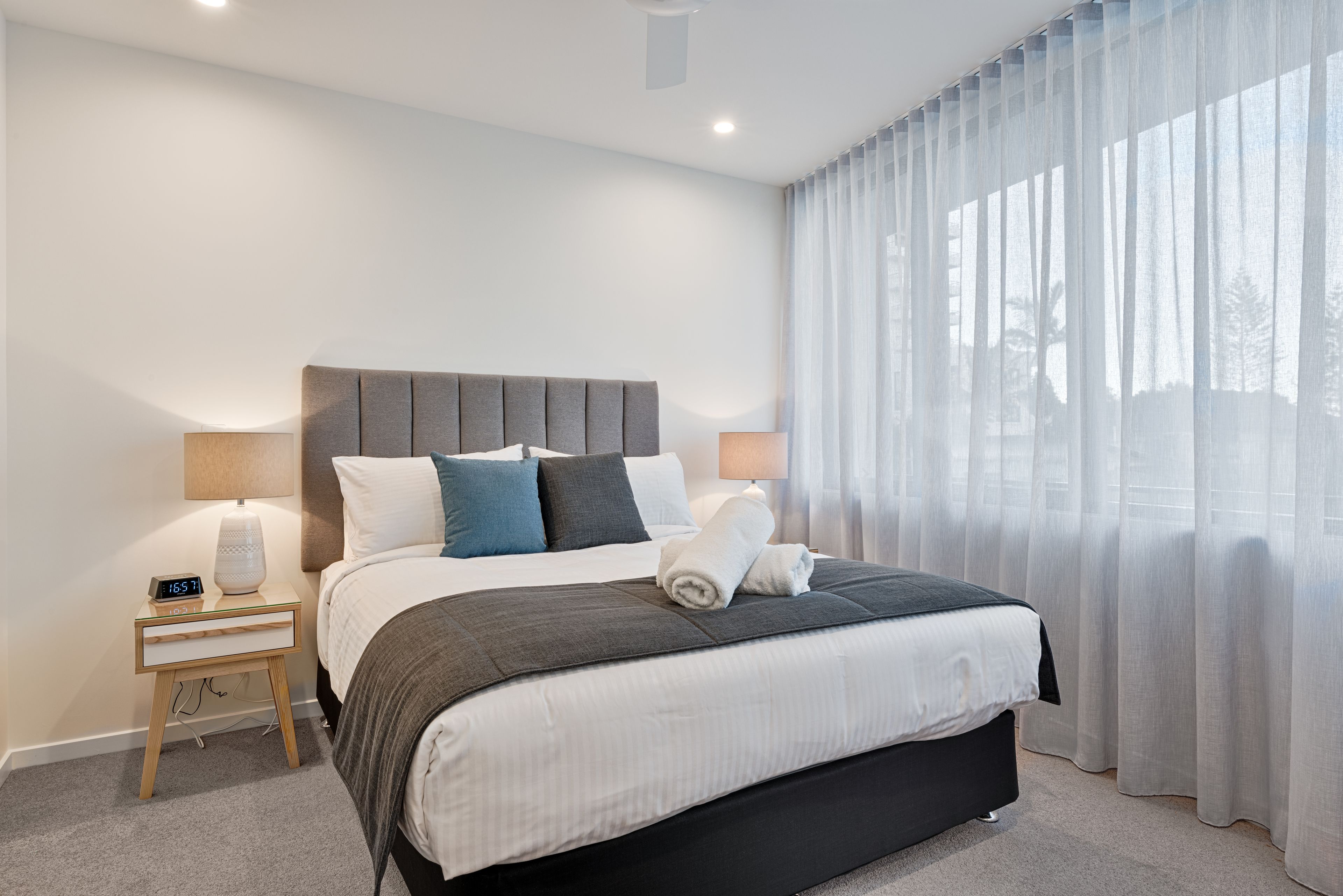 Une chambre d’hôtel moderne avec un grand lit, deux tables de chevet et une fenêtre ornée de rideaux légers.