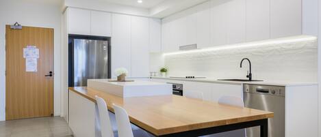 Uma cozinha moderna com armários brancos, uma geladeira de aço inoxidável, uma mesa de jantar de madeira com cadeiras e eletrodomésticos embutidos.