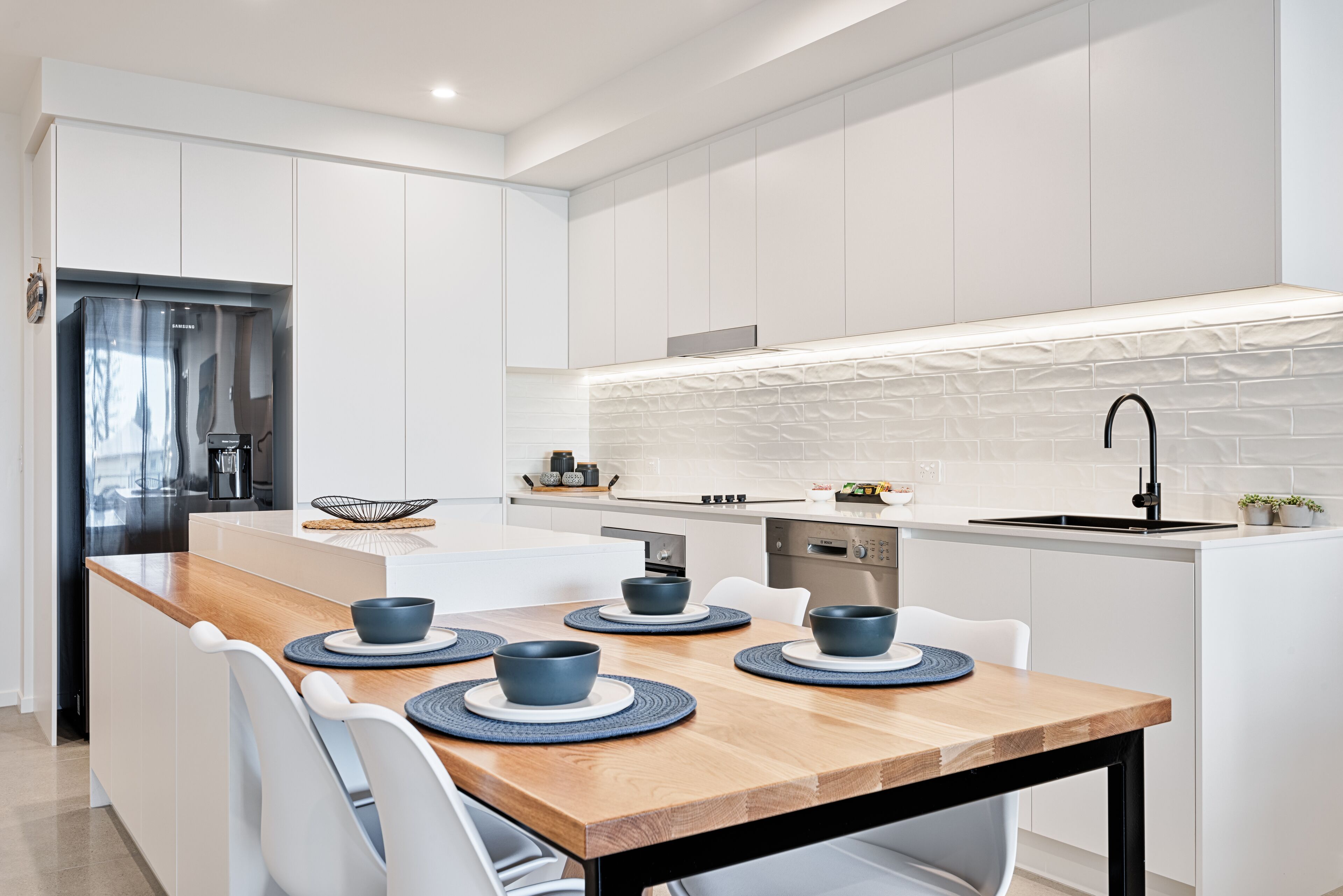 Una cocina moderna con armarios blancos, una isla de madera con asientos y una estufa empotrada.