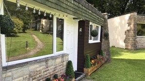 A house with a stone facade, a wooden front porch, and a garden with flower beds. - Welcome to Poldark Country - A Cornish Idyll! (Camelford)