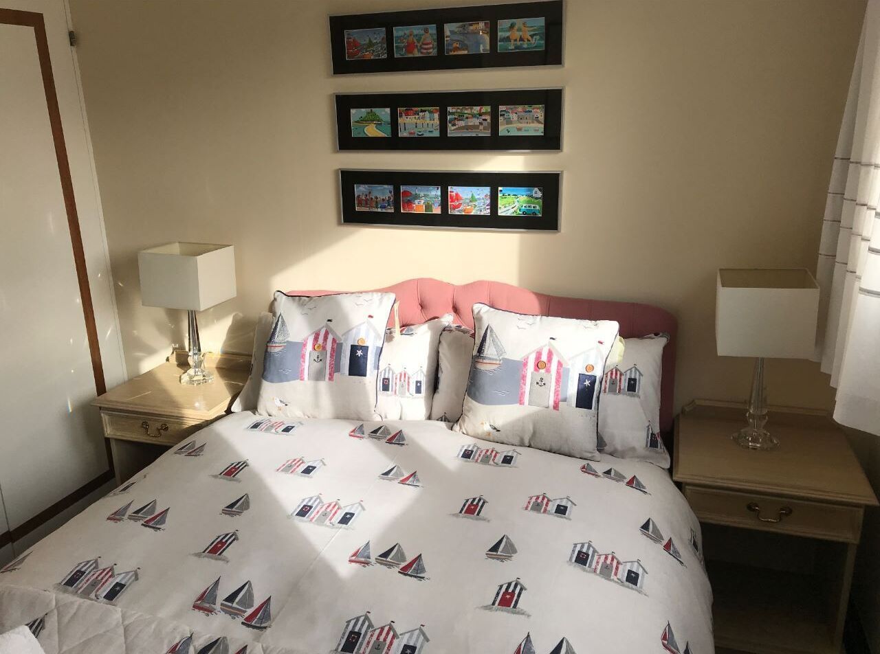 A hotel room with a bed, two bedside tables, a nightstand, a wall with framed pictures, and a window with curtains.
