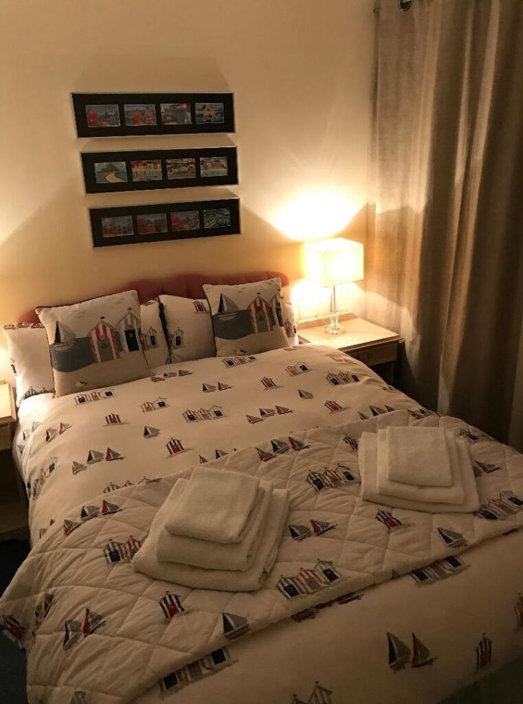 Een hotelkamer met een bed met een deken met nautisch thema, een bedlamp en een fotopresentatie aan de muur.