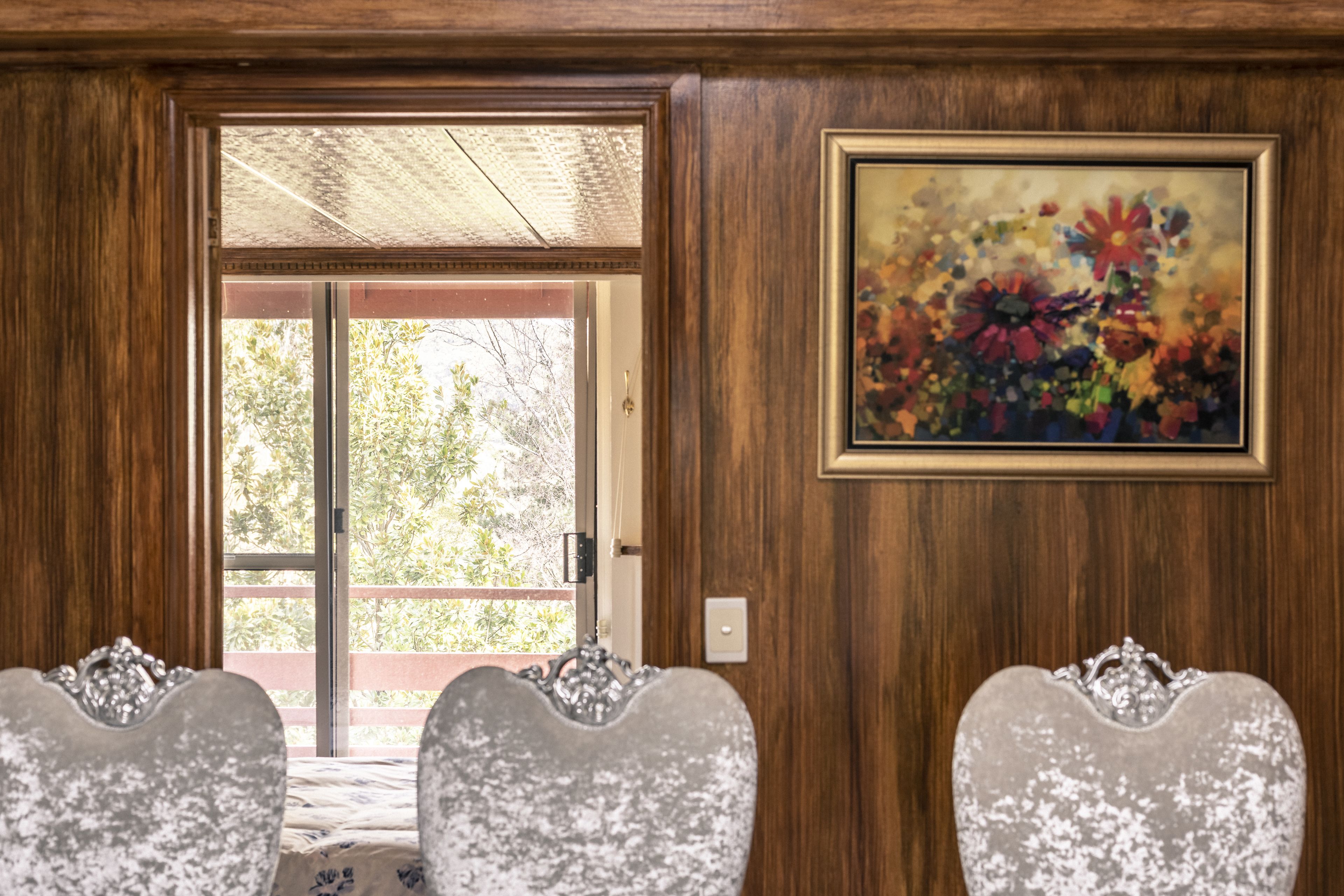 A room with a wooden door, a glass door leading outside, and a framed floral painting on the wall.