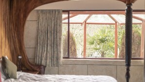 Camera da letto con un'ampia finestra, un letto con testiera in legno e vista sul verde.