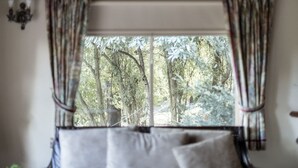 Una finestra con tende, un letto con cuscini e vista su alberi.