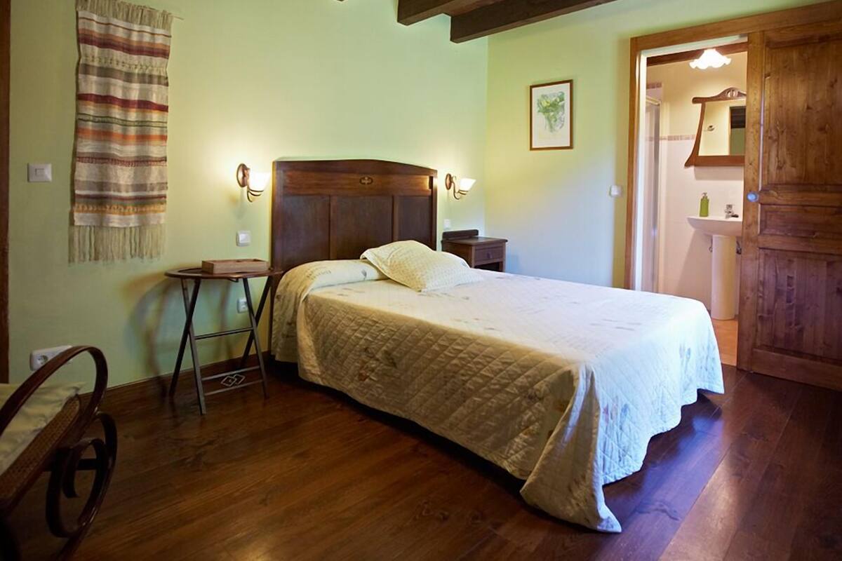 A cozy bedroom with a wooden bed, a small bedside table, a chair, and a wooden door.