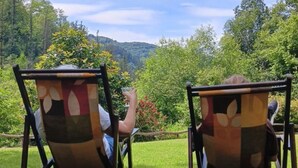 Two outdoor chairs with a patterned backrest, positioned on a grassy lawn with a view of a forested hillside. - Casa Rural Goikola (Deba)