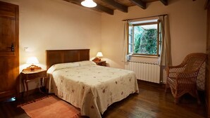 Un dormitorio con una cama de madera, una mesita de noche, una silla de mimbre, un ventanal con cortinas y techo de madera.