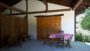 Un espacio de estar al aire libre cubierto con una mesa y sillas de madera, una puerta de madera y suelo de concreto.