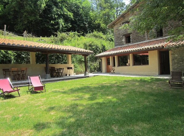 A courtyard with two covered seating areas, a stone building, and a grassy lawn.