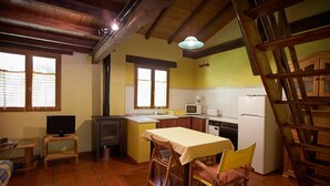 Una cocina compacta con electrodomésticos básicos, un comedor con mesa y sillas, y un televisor sobre una mesita.