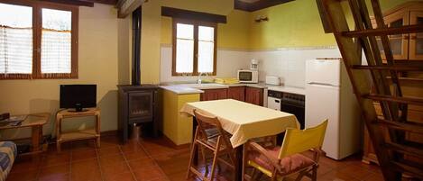 Una cocina compacta con electrodomésticos básicos, un comedor con mesa y sillas, y un televisor sobre una mesita.