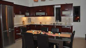 A modern kitchen with dark wood cabinets, stainless steel appliances, a granite countertop, and a dining area with a wooden table and chairs. - Porfyra's Island (Ierapetra)
