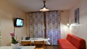 A room with a dining table, chairs, a red sofa, a TV on the wall, and a ceiling light. - Grand Cap 3 - Appt 4 pers in Chalet - CALM & NATURE (Tignes)