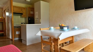A compact kitchen with wooden cabinets, a white countertop, and a dining area with a bench and table. - Grand Cap 3 - Appt 4 pers in Chalet - CALM & NATURE (Tignes)