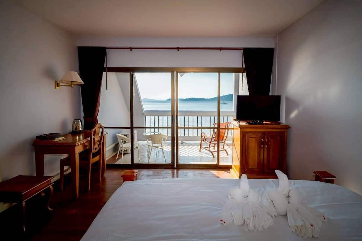 Habitación de hotel con cama, escritorio, silla, televisor y balcón con vista al mar.