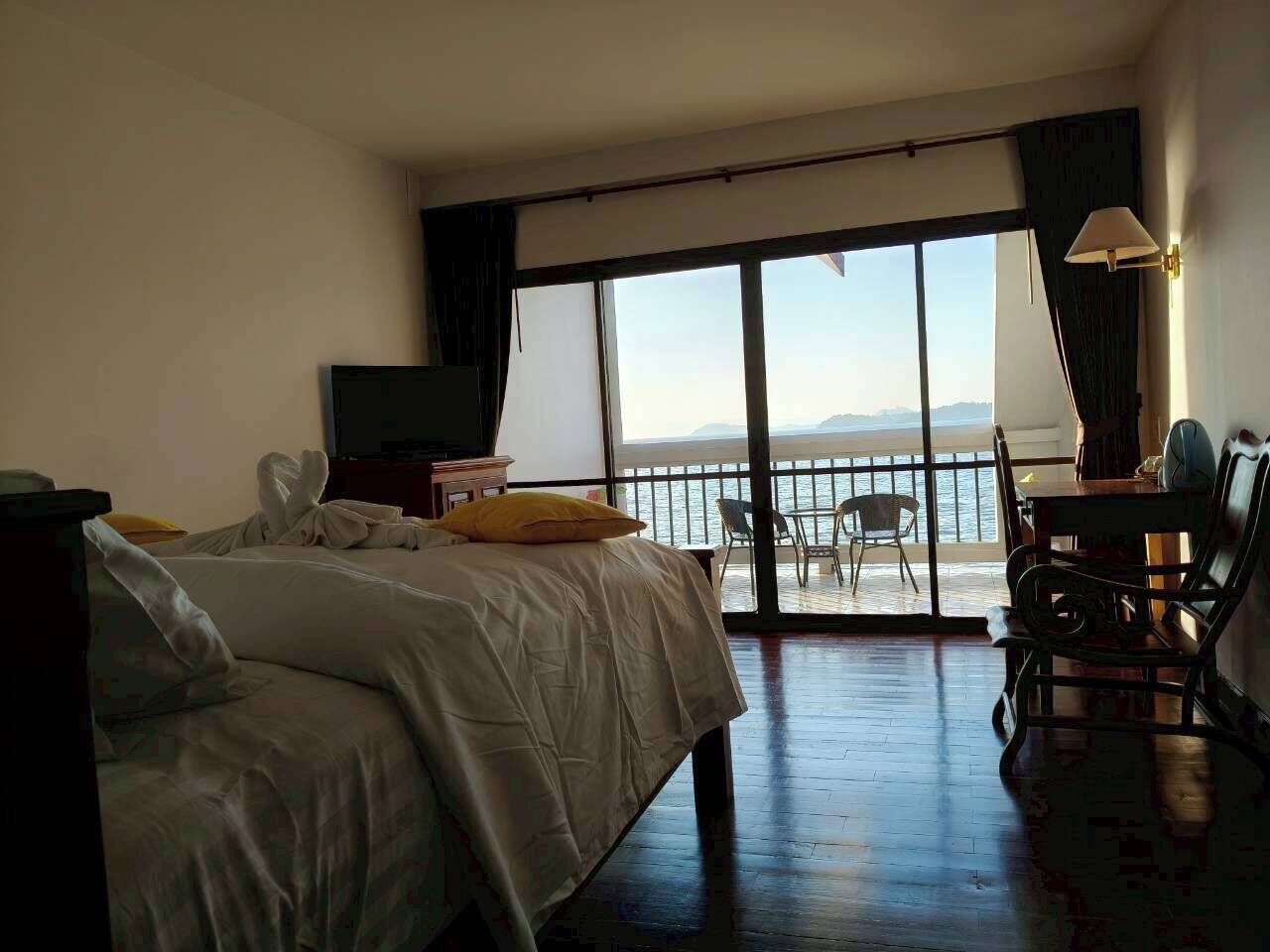 A hotel room with a bed, a TV, a desk with a chair, and a balcony with a view of the sea.