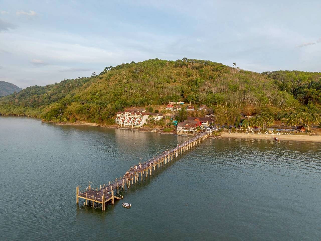 Une jetée s’avançant dans un lac, avec un bâtiment et une plage en arrière-plan.