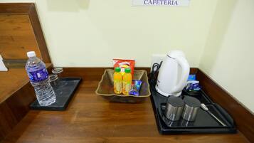 Zona de recepción de hotel con una botella de agua, jugo, bocadillos, una cafetera y una bandeja con cubiertos.