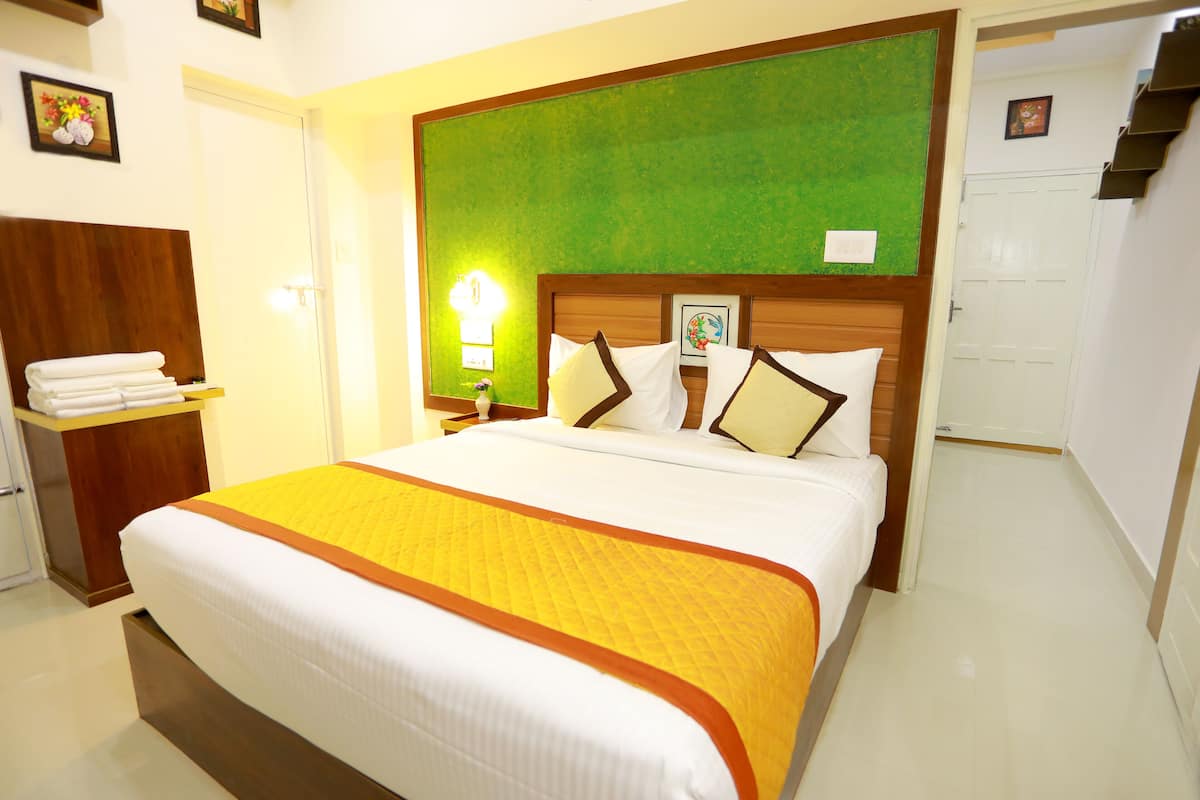 A hotel room with a large bed, a wooden headboard, a green accent wall, and a white door.