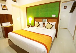 A hotel room with a large bed, a wooden headboard, a green accent wall, and a white door. - Base9 Airport Hotel (Aluva)